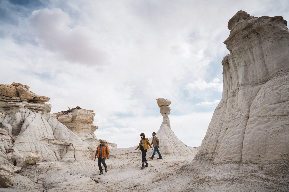 Three people wearing outdoor exploration clothing walk amongst the towering white stone structures