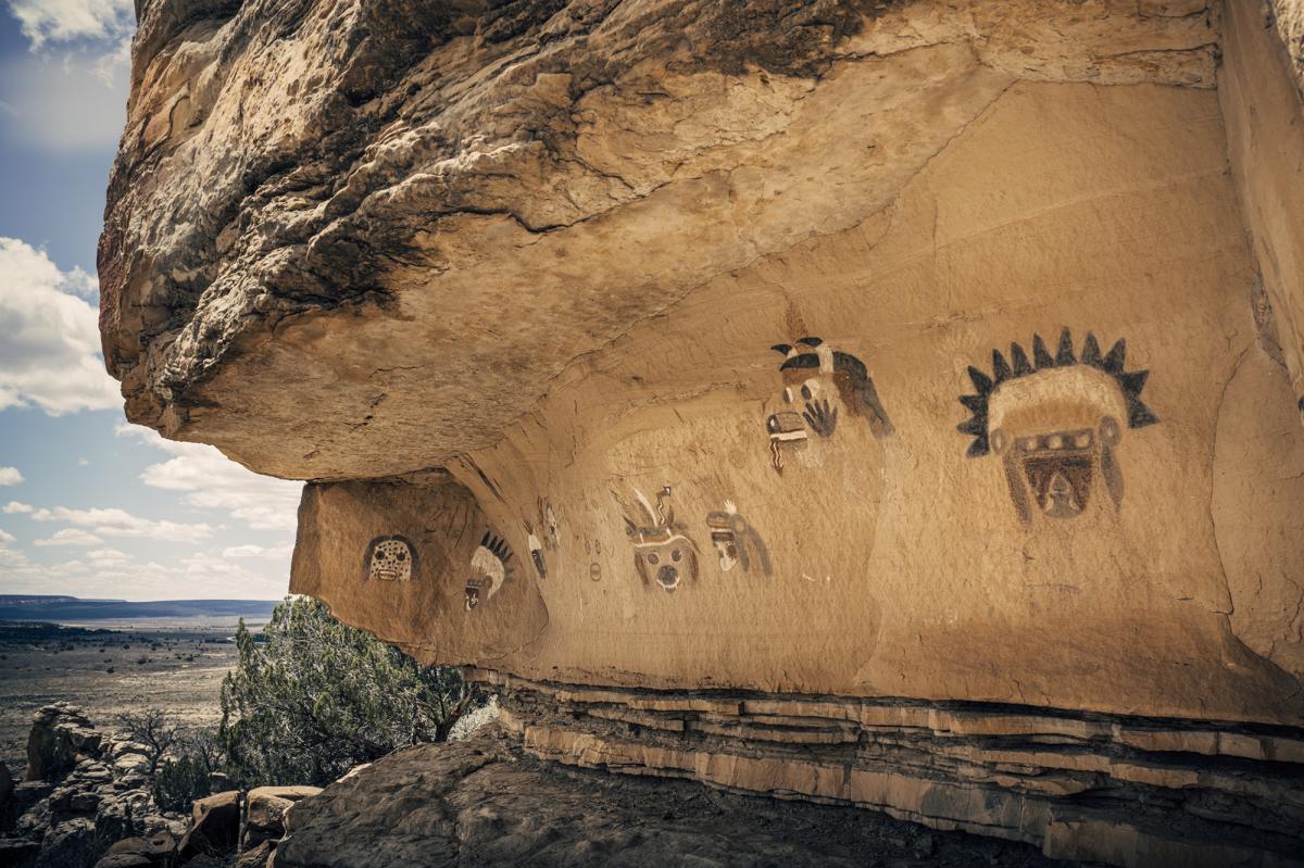 Ancestral petroglyphs adorn a cliff overhang with shrubbery around the base