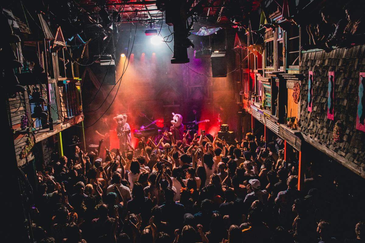 A crowd enjoying a concert at Meow Wolf in Santa Fe, illuminated by colorful nightclub lights.