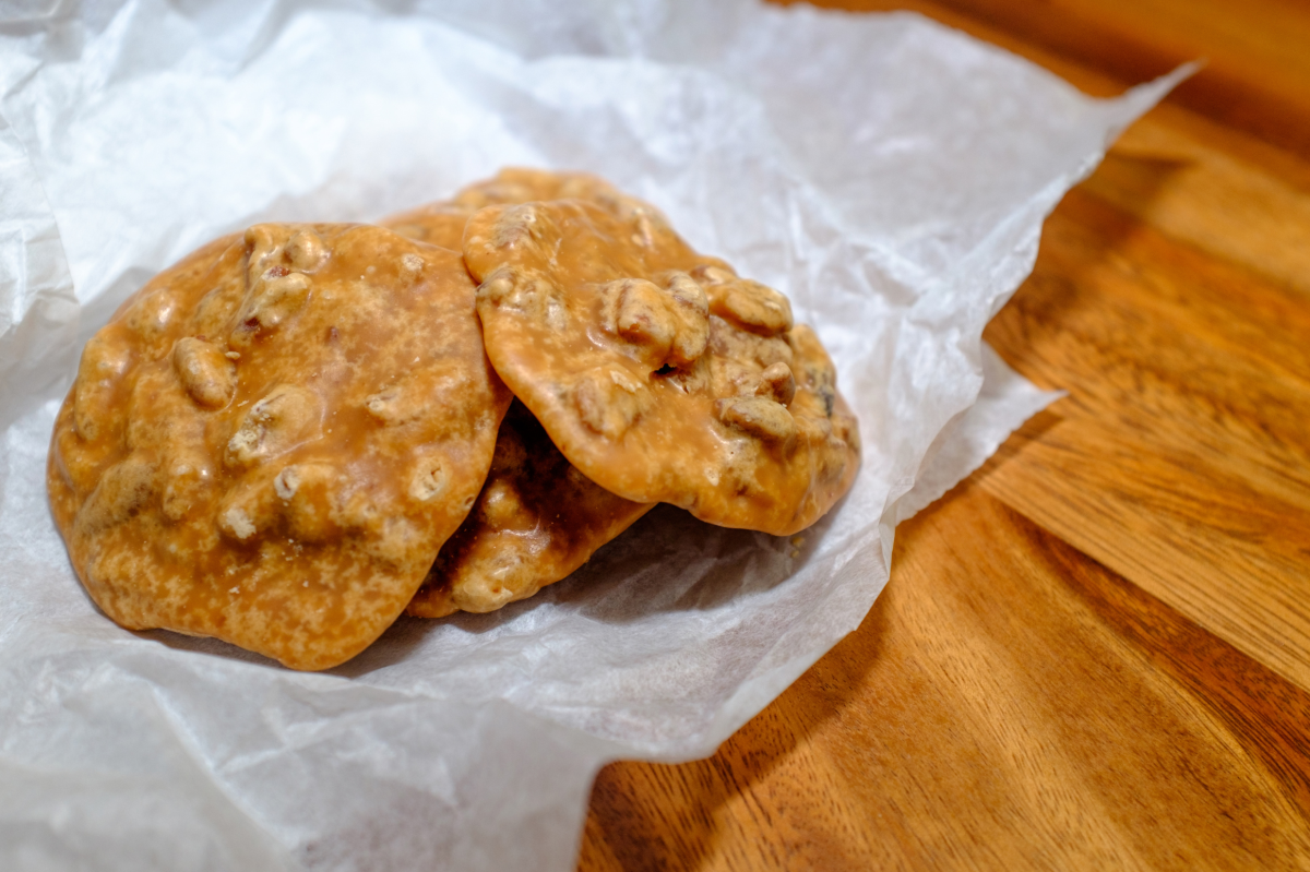 Three pecan pralines sit on a piece of white parchment paper on a wooden table.