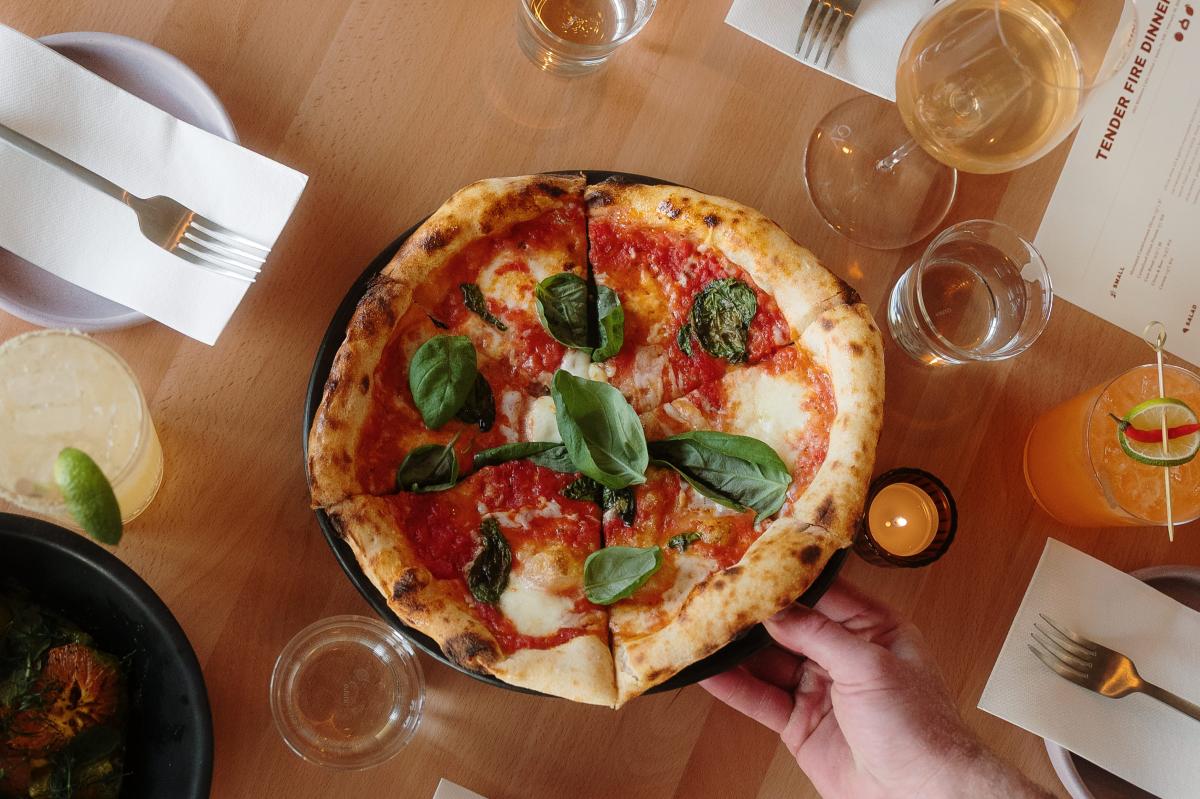 A wood-fired margherita pizza with charred crust, melted mozzarella, and fresh basil leaves.