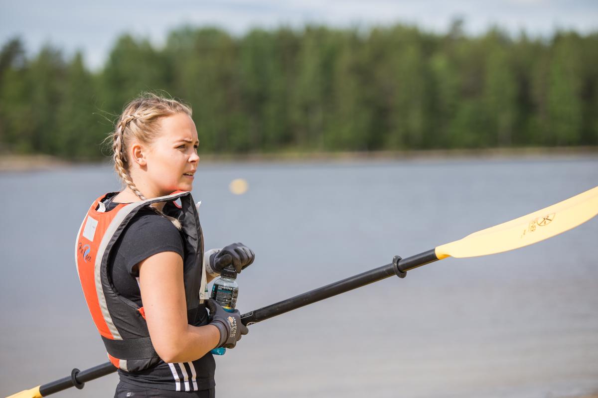 Dame står klar med padlevest og padleåre mens hun skuer utover sjøen.