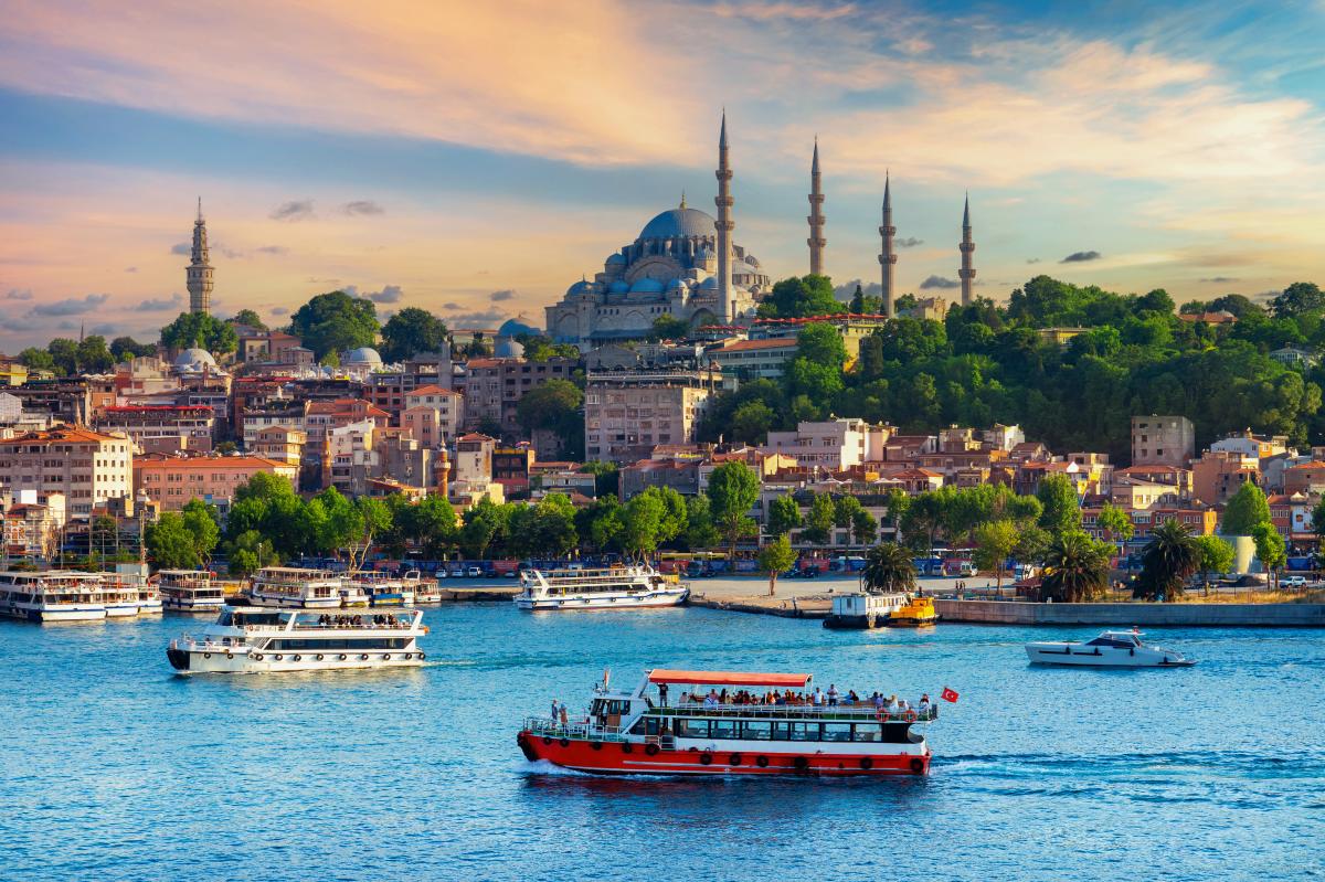 A scenic view of Istanbul, Turkey, at sunset. The iconic Sultan Ahmed Mosque, also known as the Blue Mosque,dominates the skyline. Boats are sailing on the Bosphorus Strait, with the city's historic buildings and colorful houses visible in the background.