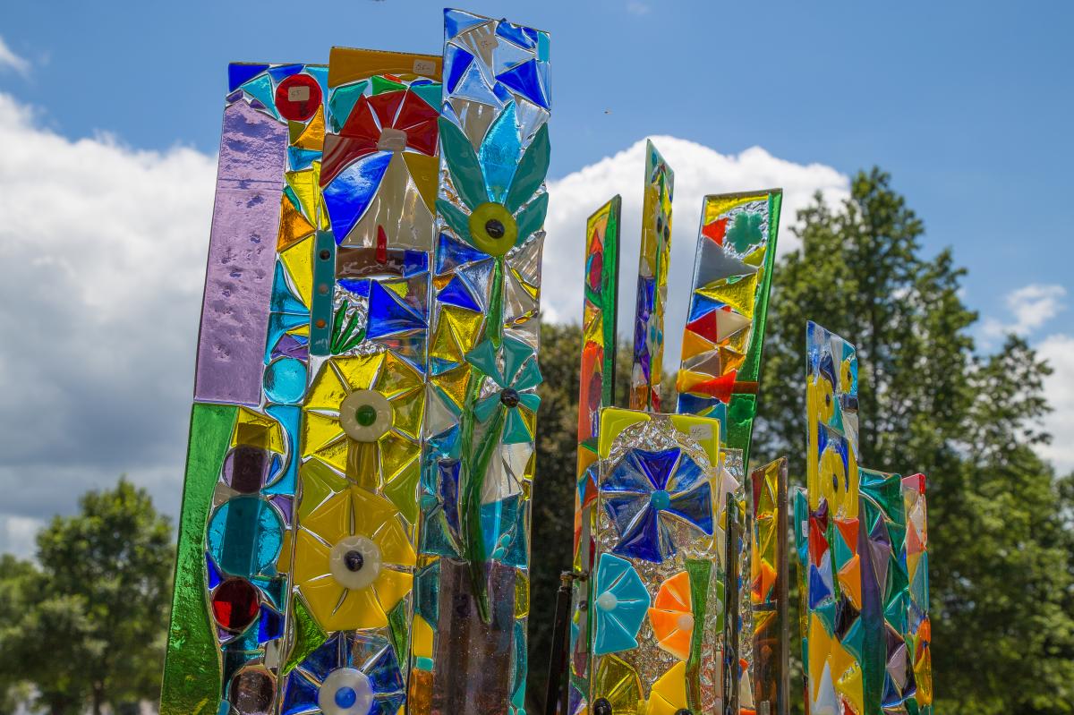 Colorful glass art panes in front of a blue sky with clouds and trees in the background