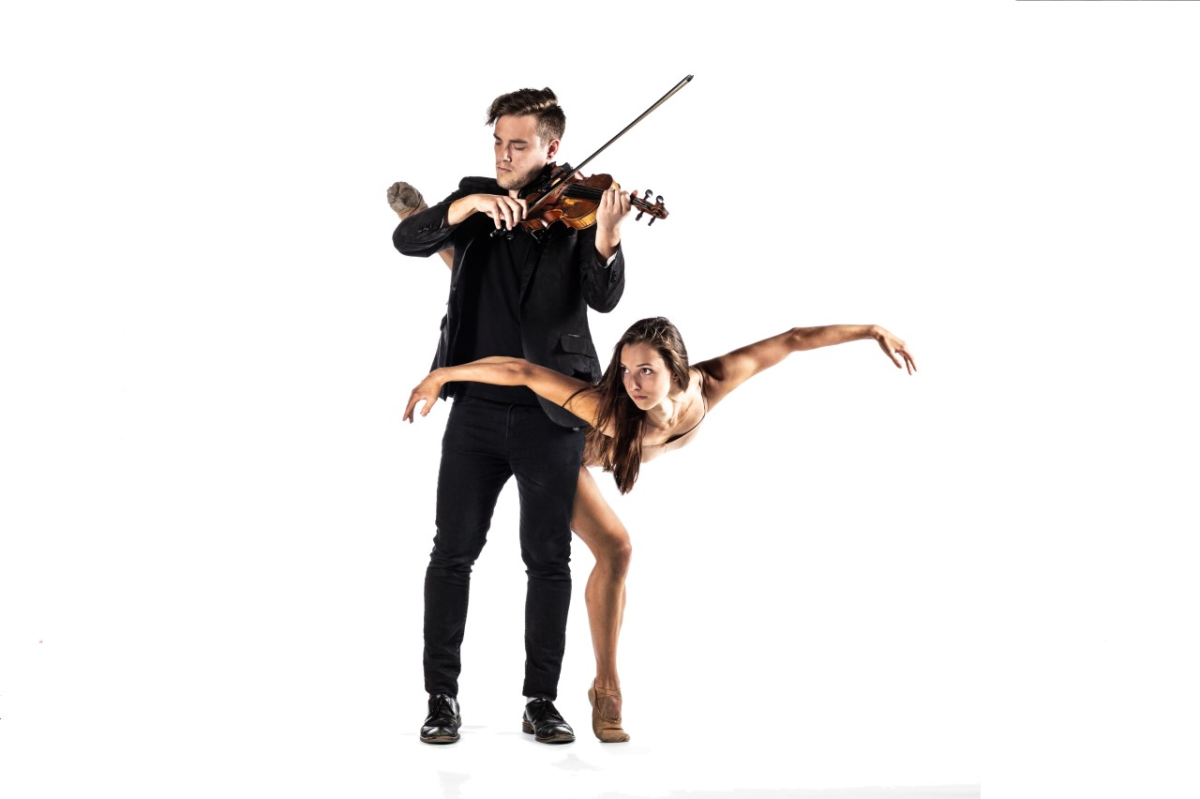 A man playing the violin while a woman dances around his back.