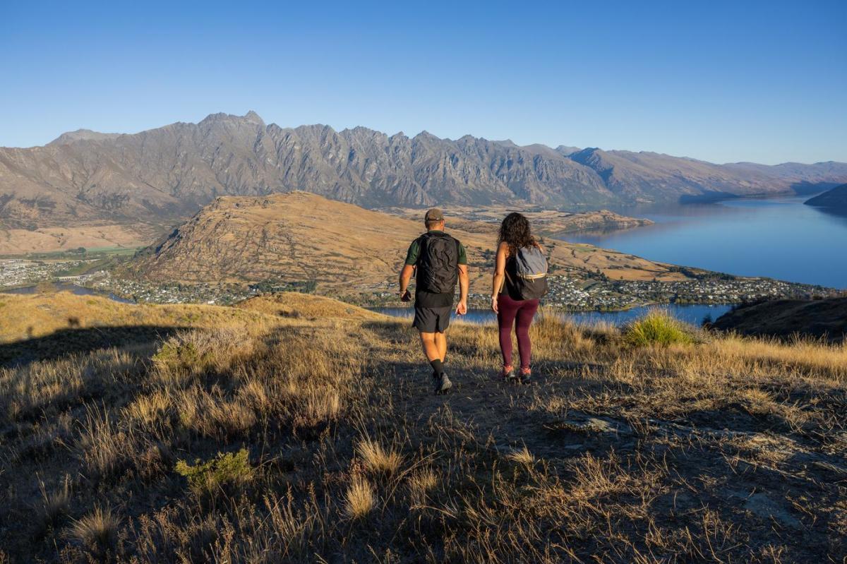 Two people walking with the Remarkables mountain range in the background