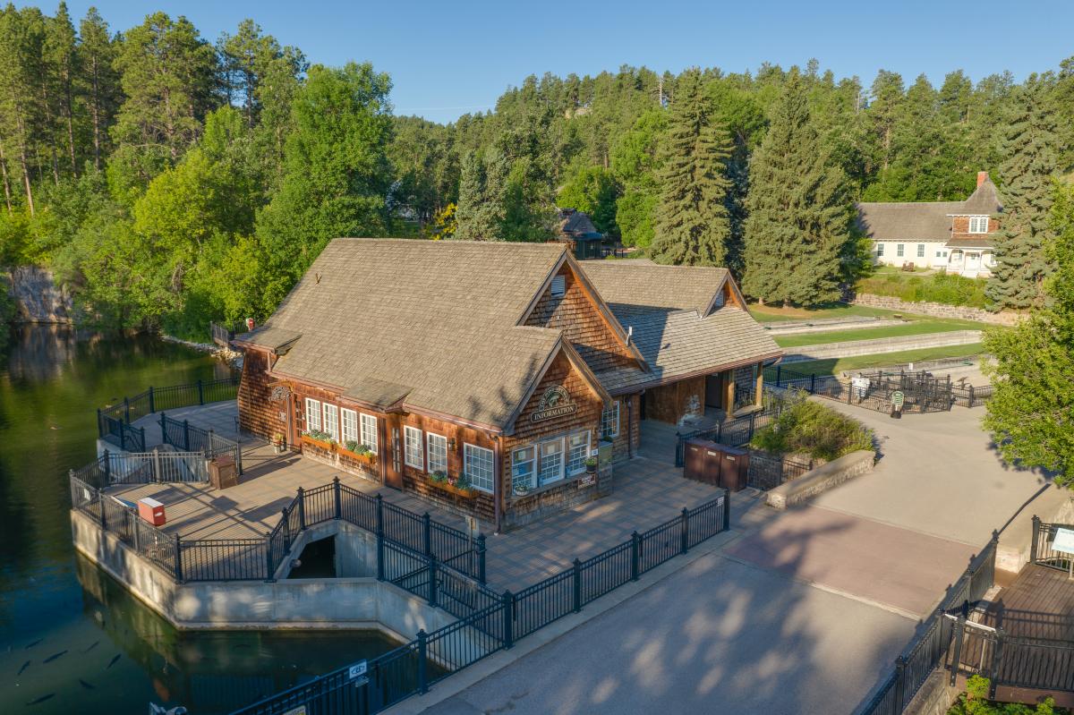 A drone photo of the main building at the DC Booth Fish Hatchery in Spearfish, surrounded by pine trees, concrete walk paths, and a large pond to the left.