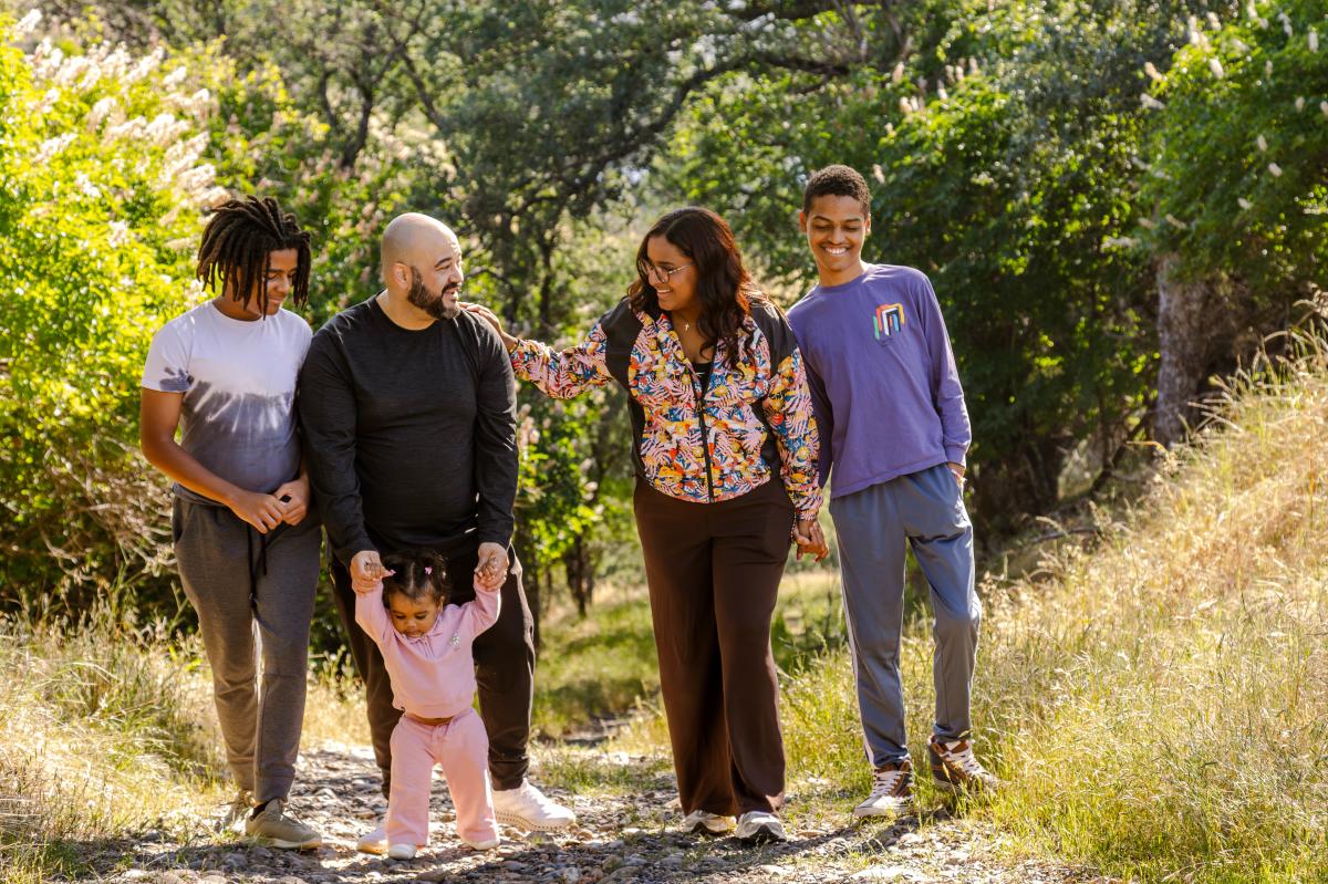 Family pictured hiking in a forested and shaded trail.