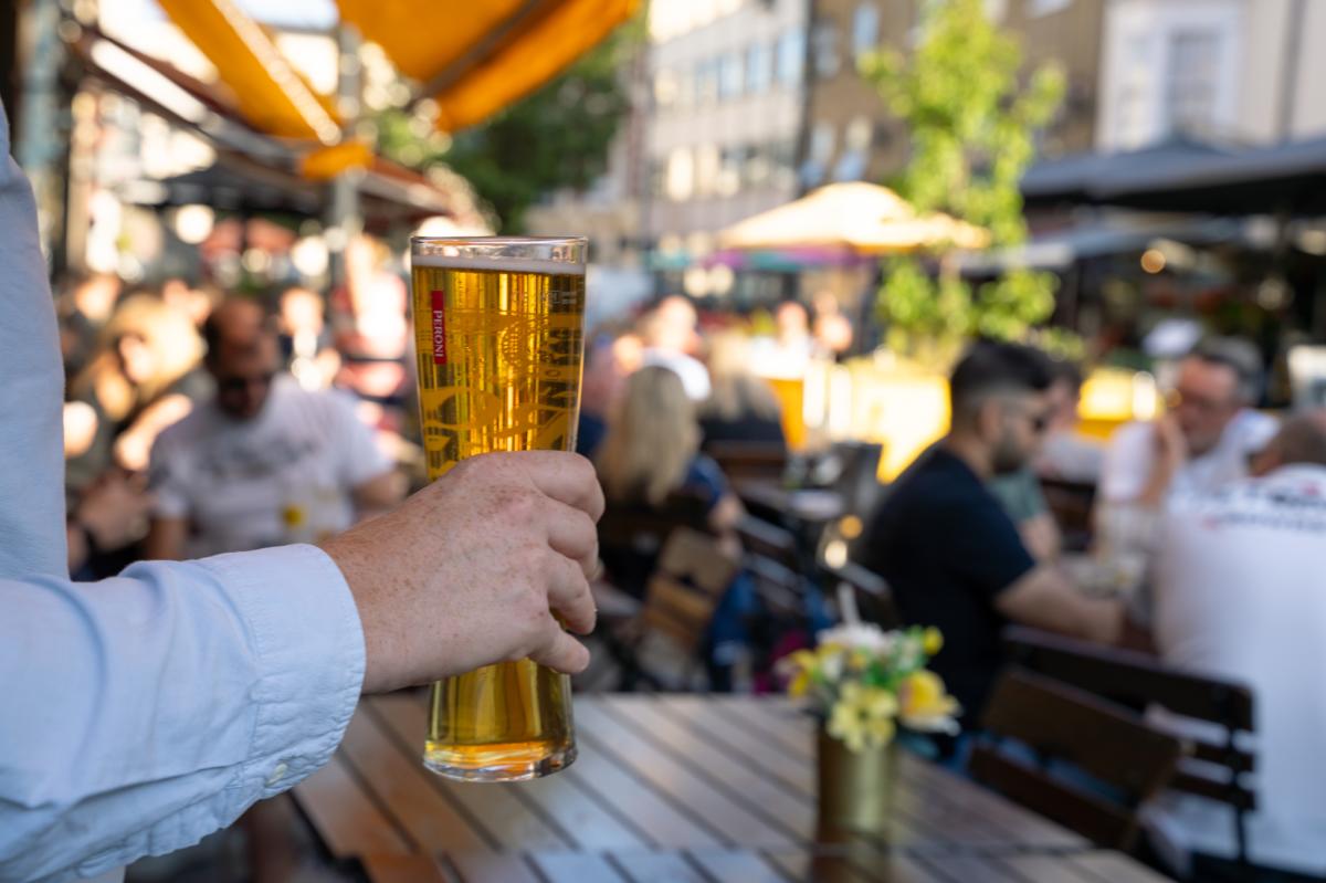 Man holding up a pint of beer sitting on an outdoor terrace on Oxford Street
