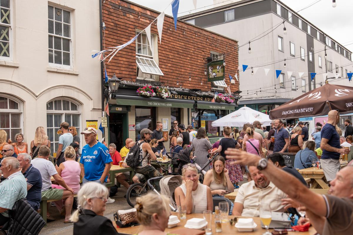 Crowds of people sitting outside on benches enjoying food and drink at Bedford Place Summer Festival
