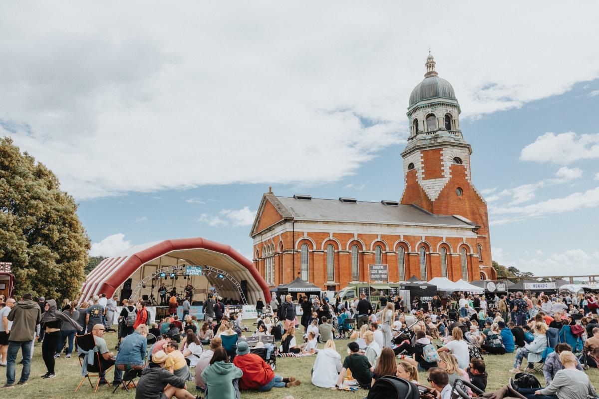 Groups of people sitting on grass in front of stage or walking around the grounds of Royal Victoria Country Park at The Big Eat Festival