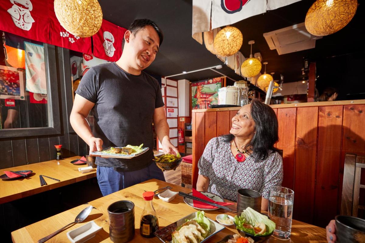 Woman smiling a man serving Japanese dishes to table at Sakura restaurant