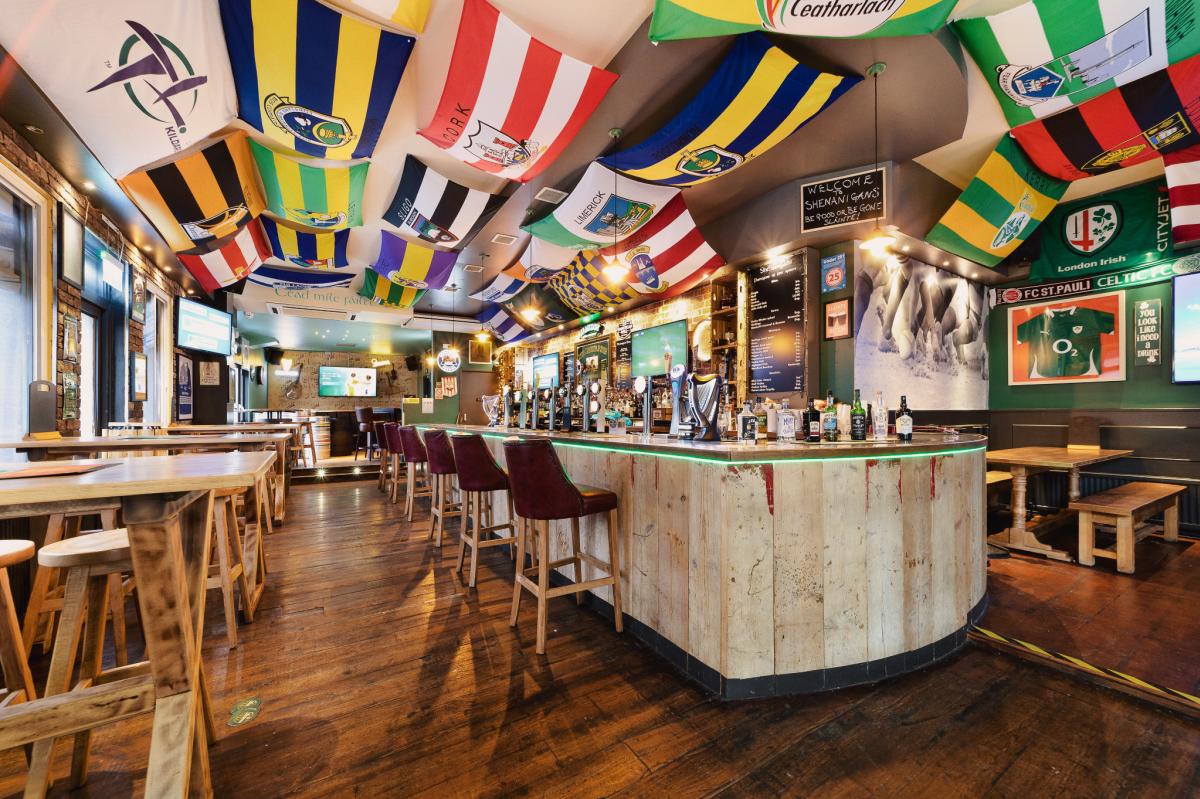 Inside of Shenanigans Irish bar with high tables and flags on the ceiling.