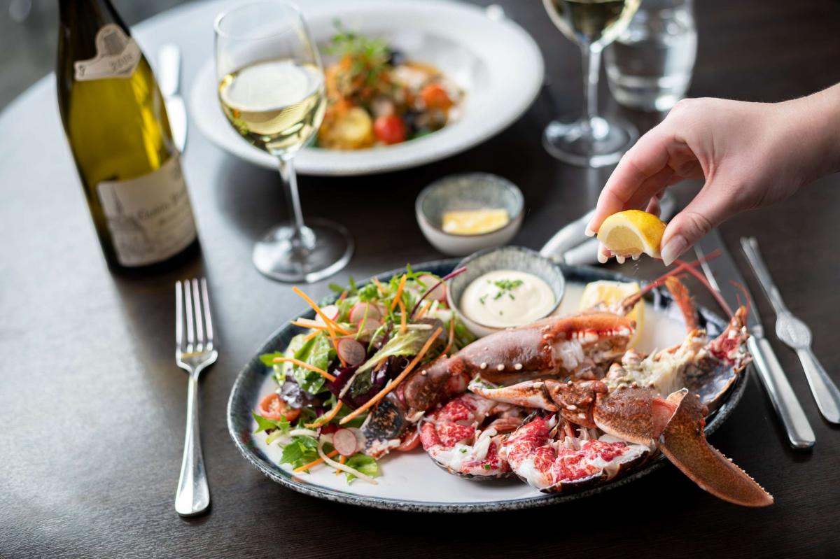 Person squeezing fresh lemon wedge on fresh lobster dish at The Jetty
