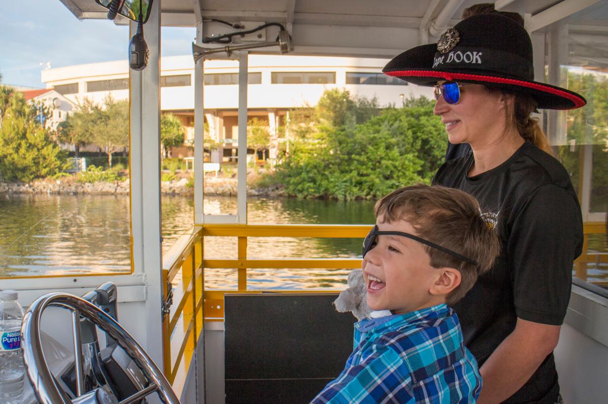 A kid wearing an eye patch and helping steer the Pirate Water Taxi boat.
