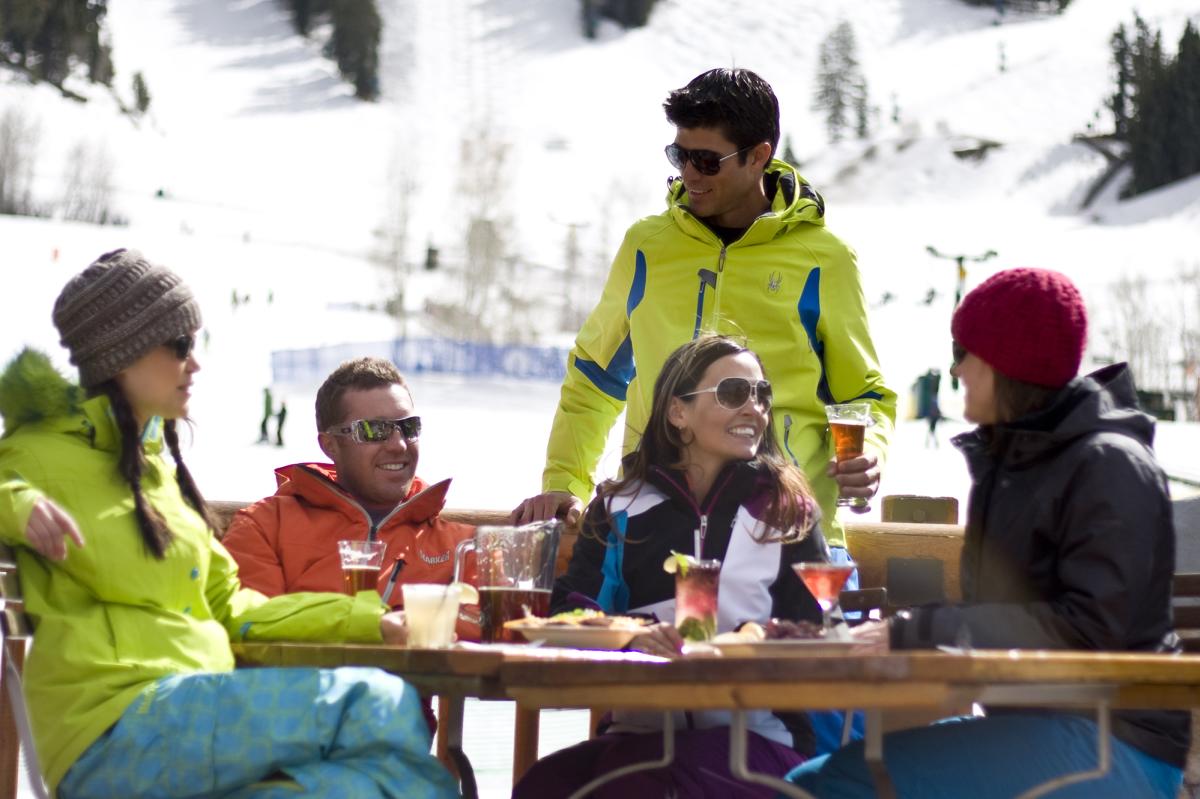 Men and Women gathered around an outside table eating at a table at a ski resort