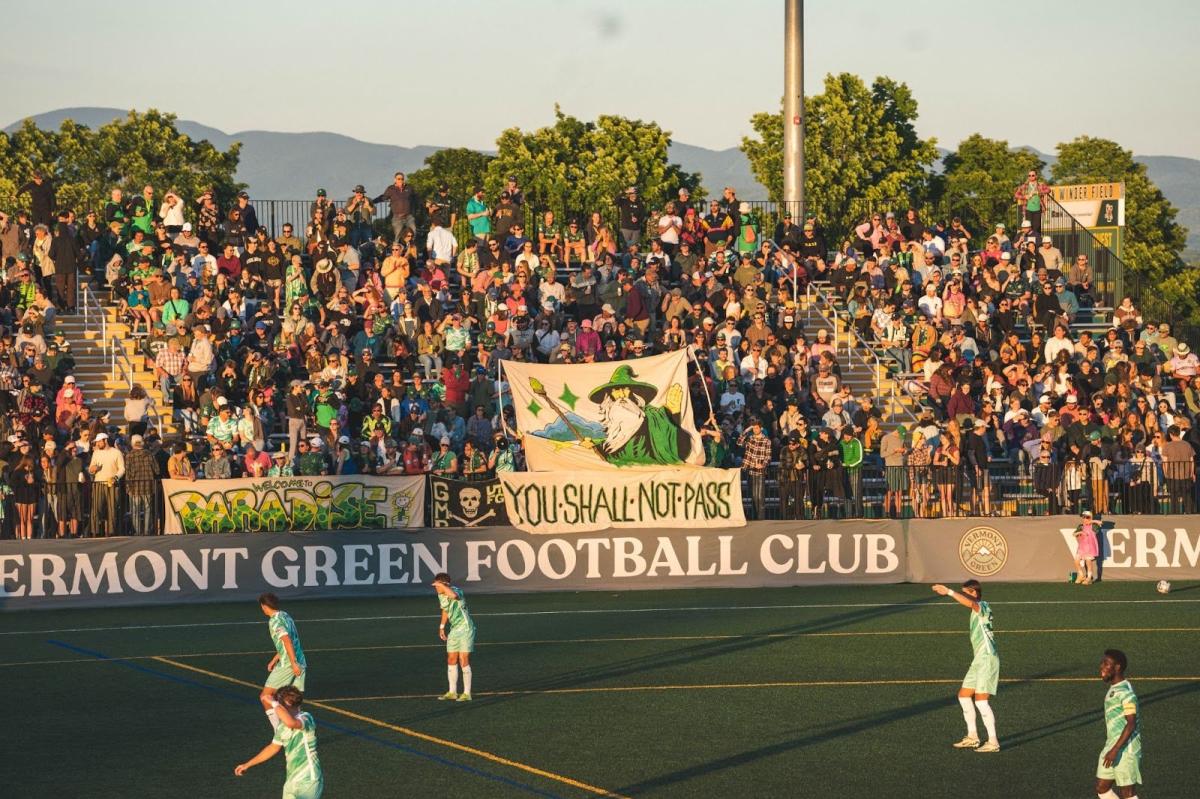 Vermont Green FC players on Virtue Field at sunset with the bleachers in the background.