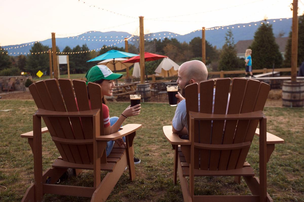 A couple cheers their beers in front of the Blue Ridge Mountains at Blue Mountain Brewery
