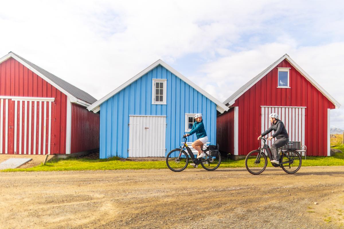 En mann og en kvinne på sykkel foran båthus i Farsund