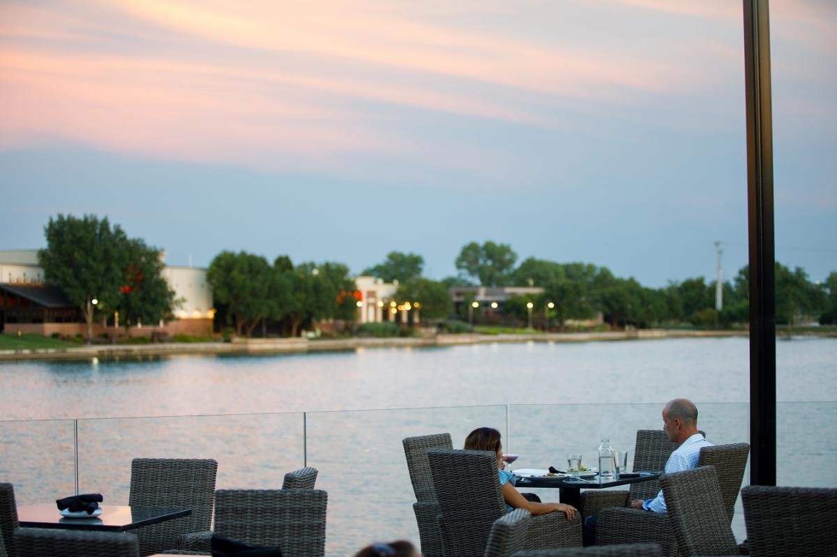 Two people enjoy glasses of wine and a meal on the patio overlooking a pond at Chester's Chophouse