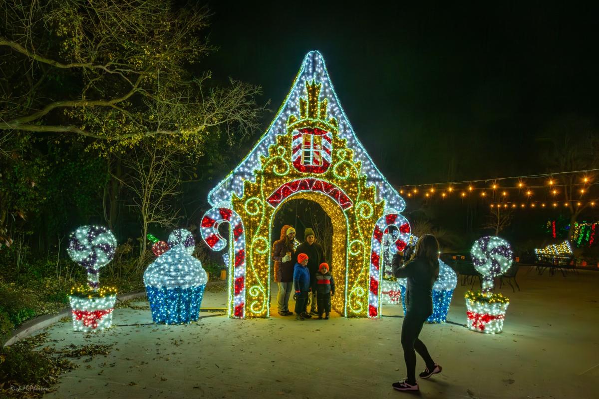 People pose in the doorway of a lit gingerbread house at botanica's illuminations