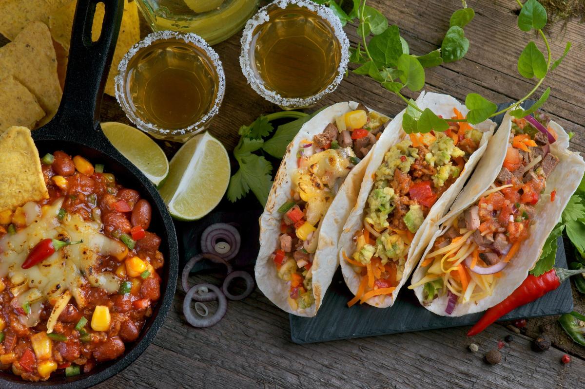 Tacos beans and shots of tequila are served on a wooden table