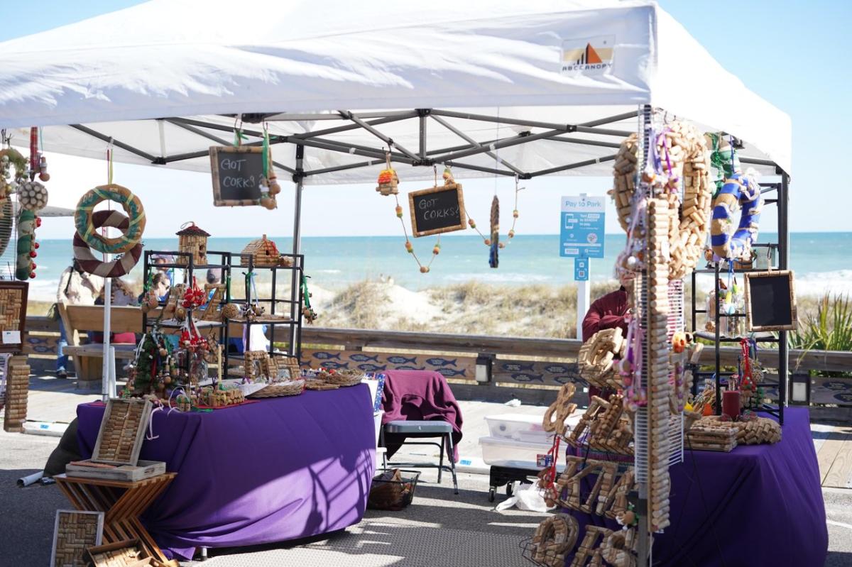 a white pop-up tent displays a variety of home decor and creations at the Kure Beach Holiday Market