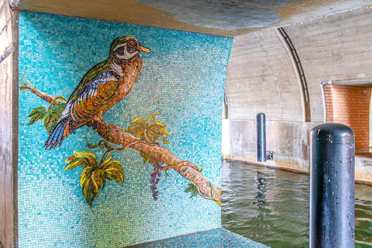 A large square mosaic of a duck under the Waterway Ave. Bridge.
