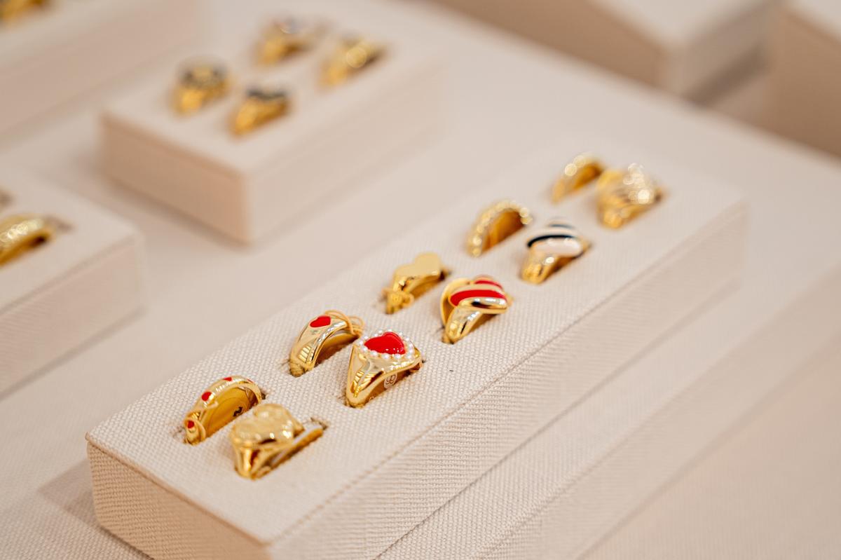 A display at gorjana features several rows of women's rings. The front two rows are primarily heart-shaped, made of gold, and set with red, white, or black enamel.