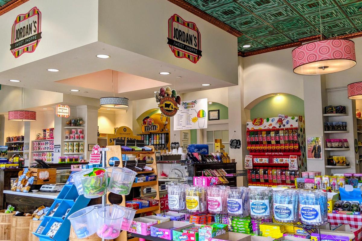 The interior of Jordan's Sweet Shoppe features row upon row of colorful candies, including rock candy sticks, boxes of nerds, M&M and jellybean dispensers, pint-sized tubs of cotton candy, etc. There are also signs advertising truffles and chocolates, Blue Bell Ice Cream, and Hawaiian Shave Ice. The ceiling tiles are bright green and black squares (like an optical illusion), and the hanging lamps are bright pink with circles made of black and white polka dots.