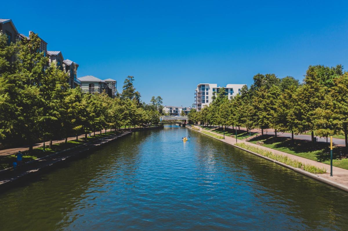 The Woodlands Waterway during the spring, with green trees along the walkways and a kayak in the water.