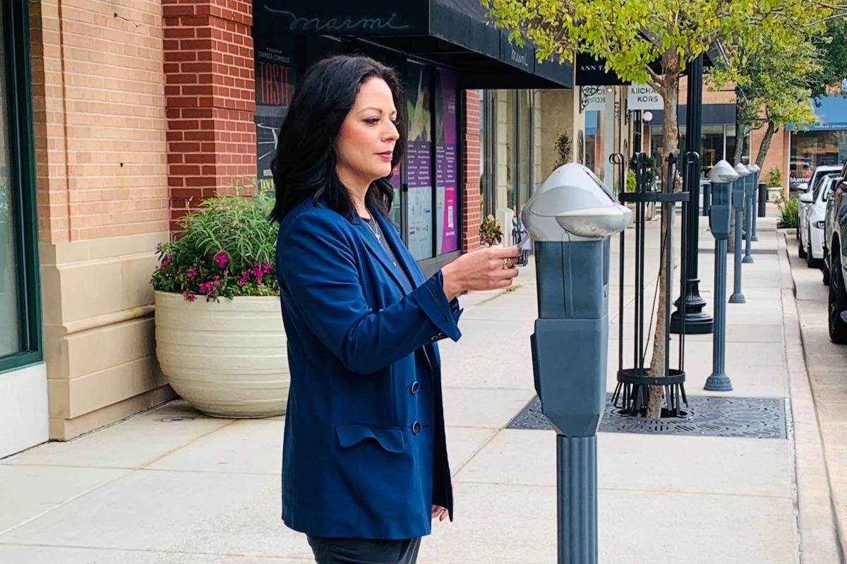 A woman with dark hair and a royal blue blazer, Sonia Guerrero, uses a parking meter at Market Street.