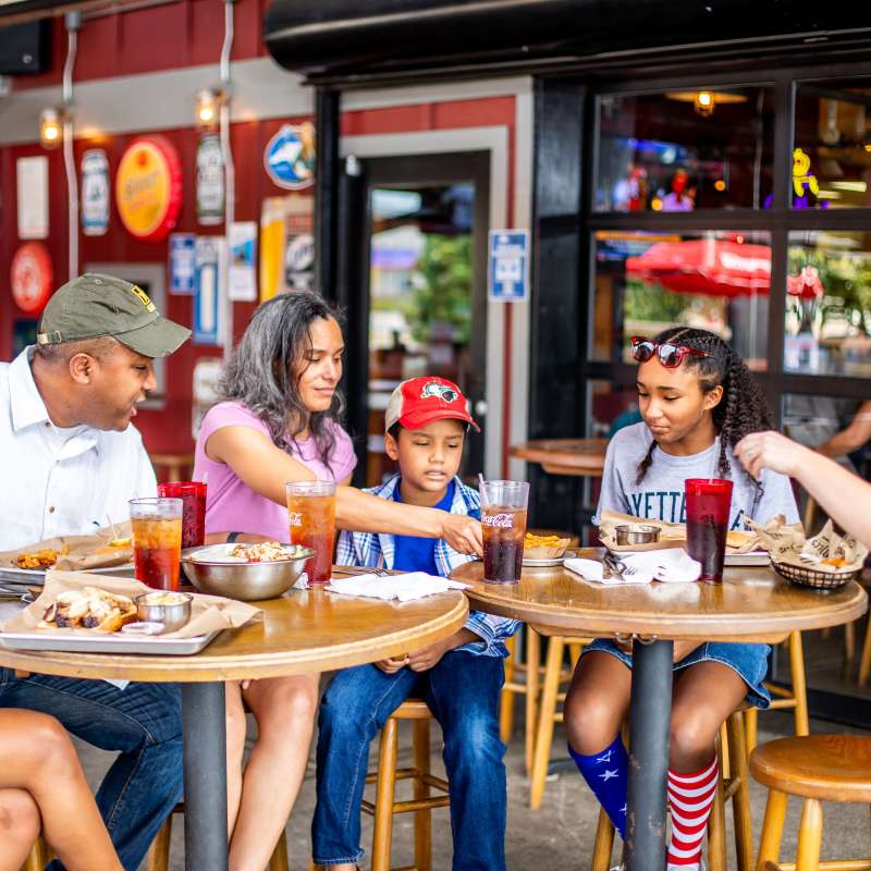 Family and friends gathered around an outdoor restaurant table sharing food and drinks together