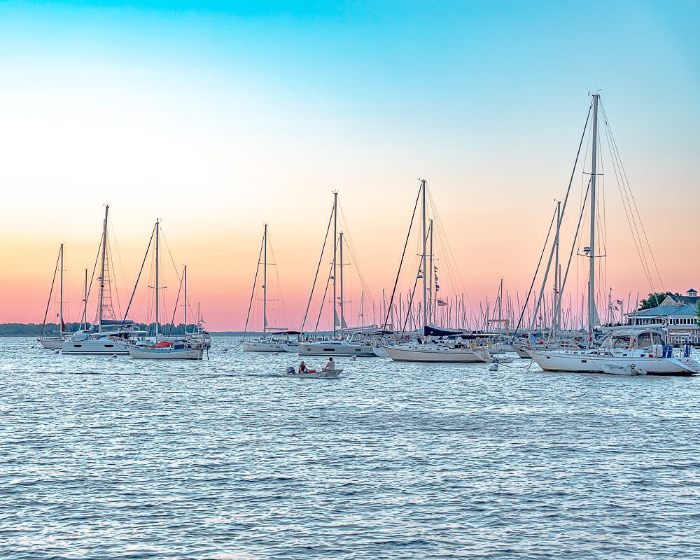 sailboats in a harbor with a sunrise in the background