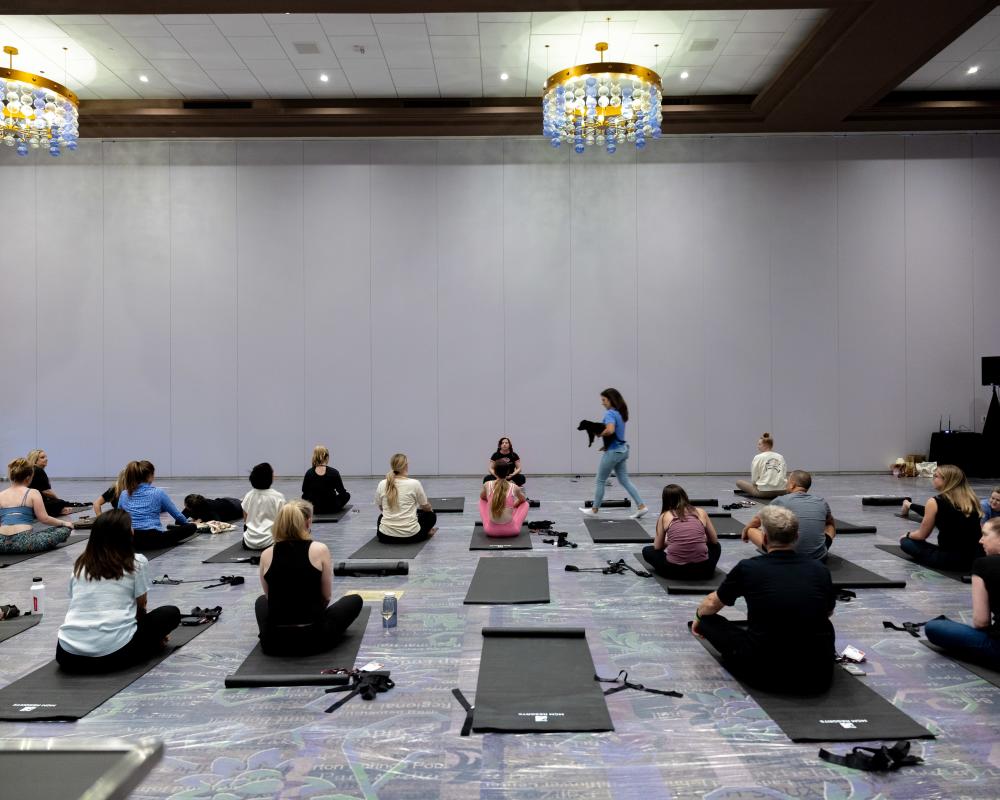 A large hotel meeting space with meeting attendees sitting on yoga mats, getting ready to take a yoga class.