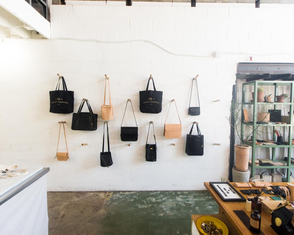 A white wall with various colored leather bags hanging on hooks at Noah Marion.