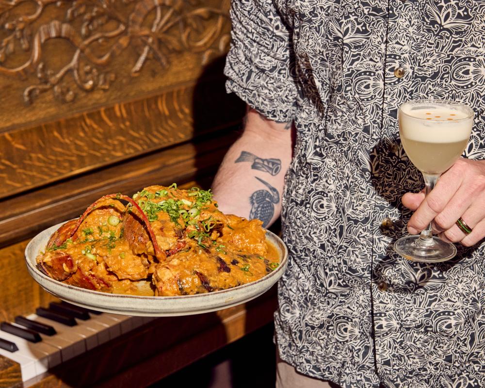 A man holding a plate of food and a cocktail at Siti.