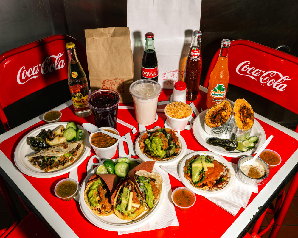 Plates of tacos, quesadillas, burritos, agua frescas and Mexican Cokes sitting on a red folding table at Taqueria de Diez.