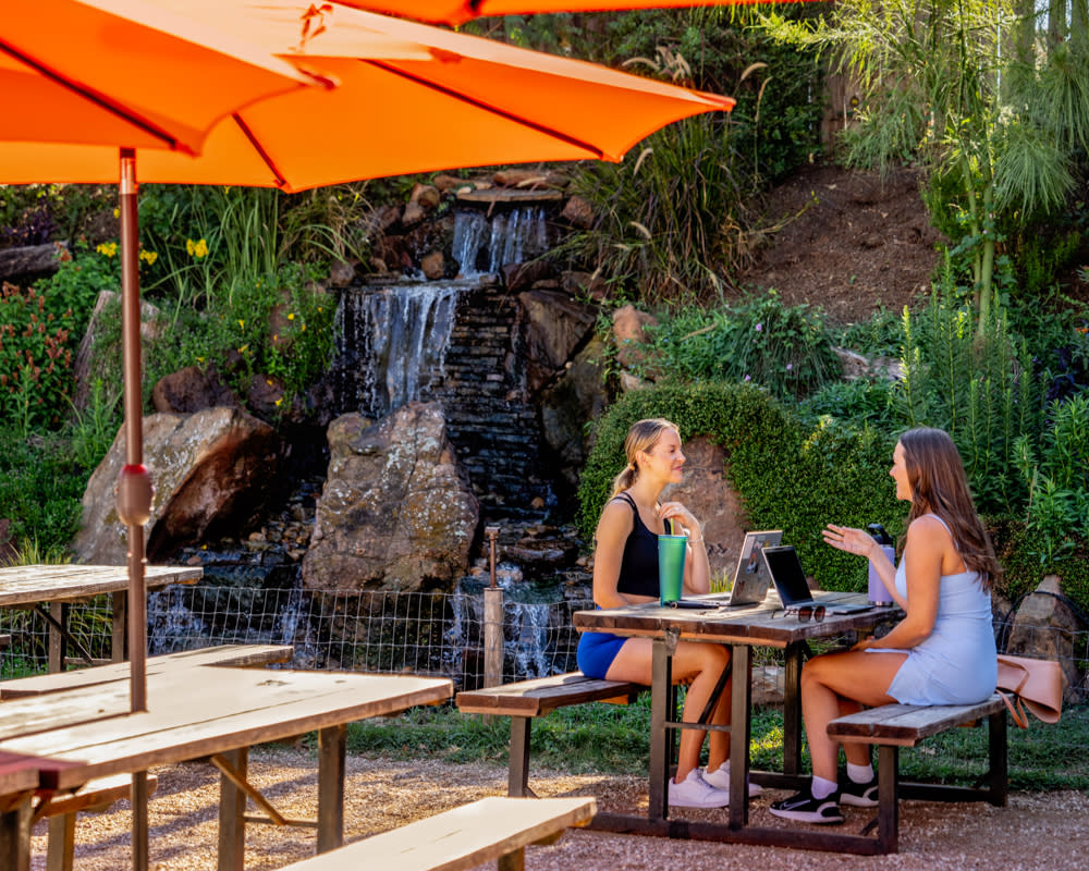Two girls sitting at a picnic table with laptops chatting at Cosmic Coffee & Beer
