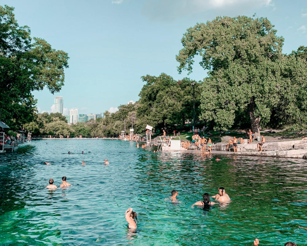 Adults and children playing in and along the banks of Barton Springs Pool.