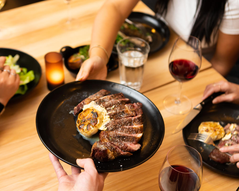 Image of someone passing off a plate of steak to someone else across the table.