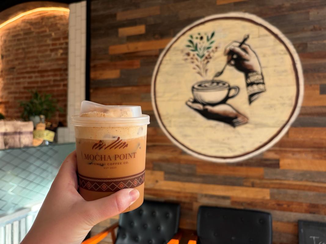 A latte from Mocha Point Yemeni Coffee being held in front of a mural inside their coffeeshop in St. Charles, MO.