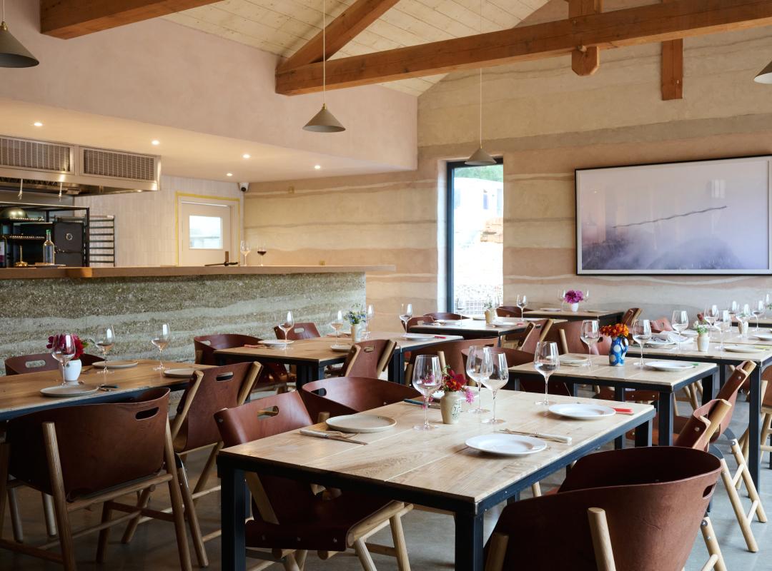 Wooden tables and chairs in the Knepp Wilding Kitchen dining room, with open kitchen to the side