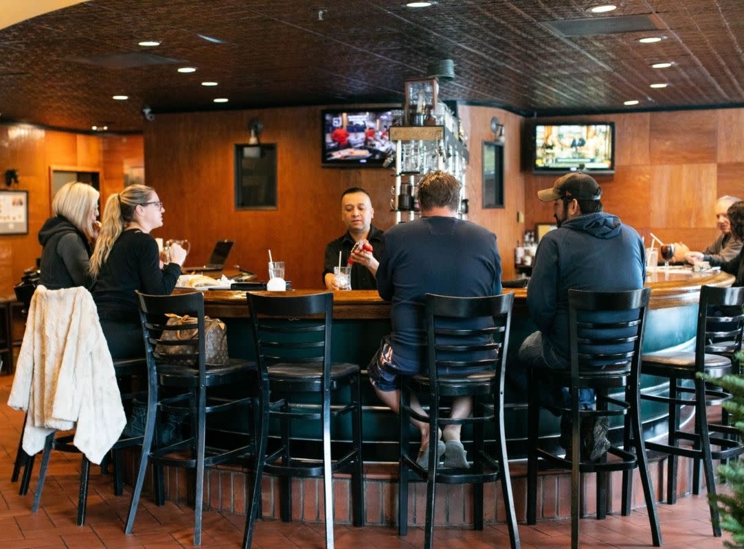 people sit at a horseshoe-shaped bar in a restaurant while a bartender makes drinks