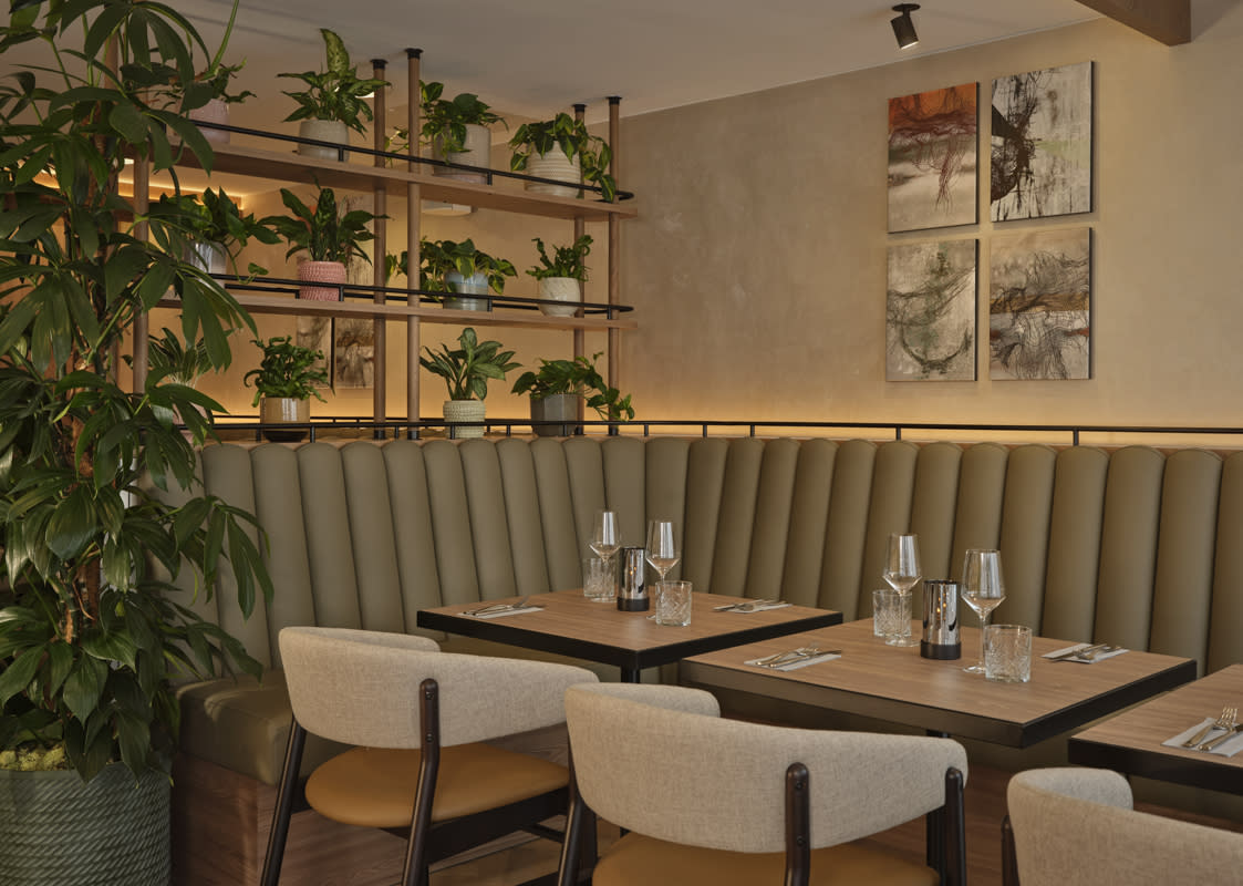 Hotel restaurant set up with glasses and cutlery with lots of plants on shelves