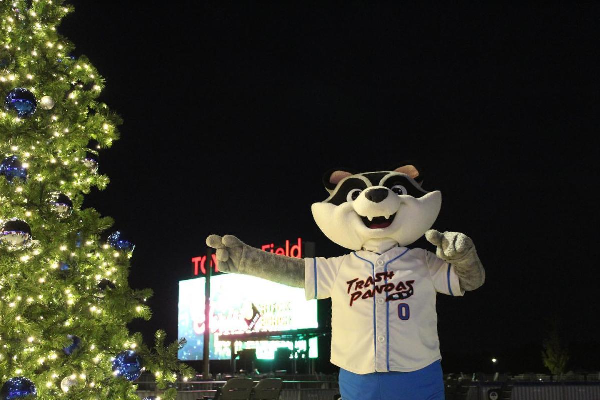 A panda mascot with a Trash Pandas jersey points to a Christmas Tree at Toyota Field