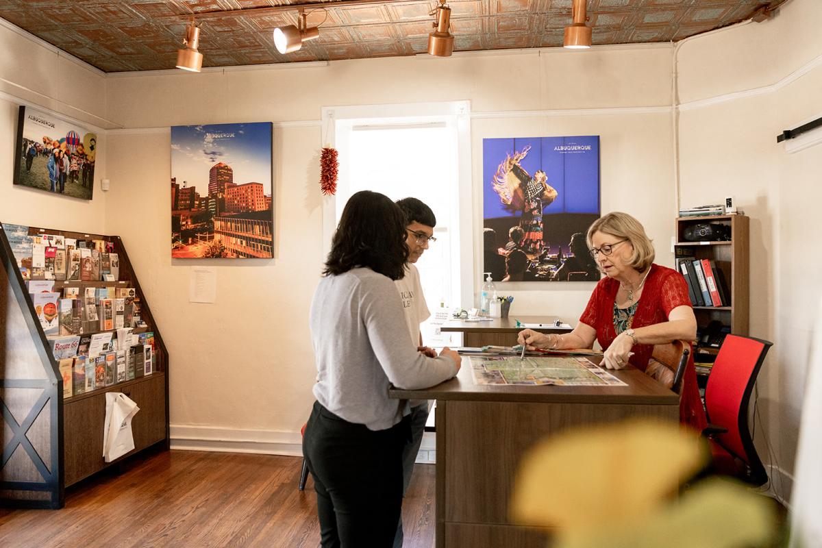 A volunteer points out something on a map to two visitors at the Visit Albuquerque Old Town Visitor Information Center.