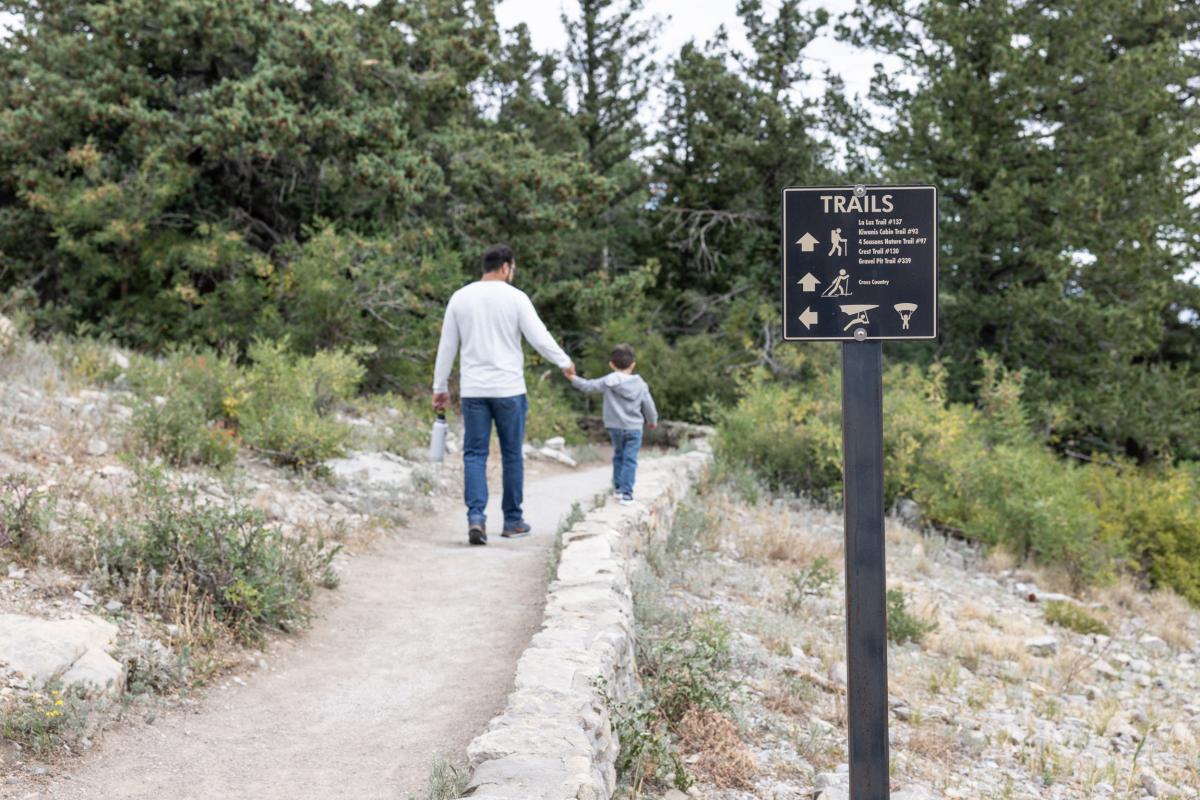 A man holds the hand of a young boy as they walk on a trail in the Sandia Mountains