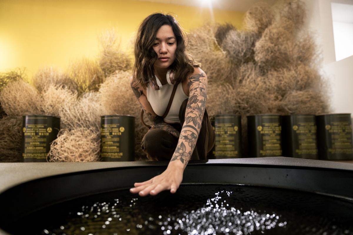 A woman interacts with a water feature in an exhibit at 516 Arts.
