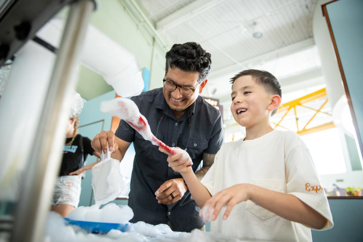 A young boy and man play with bubbles at Explora
